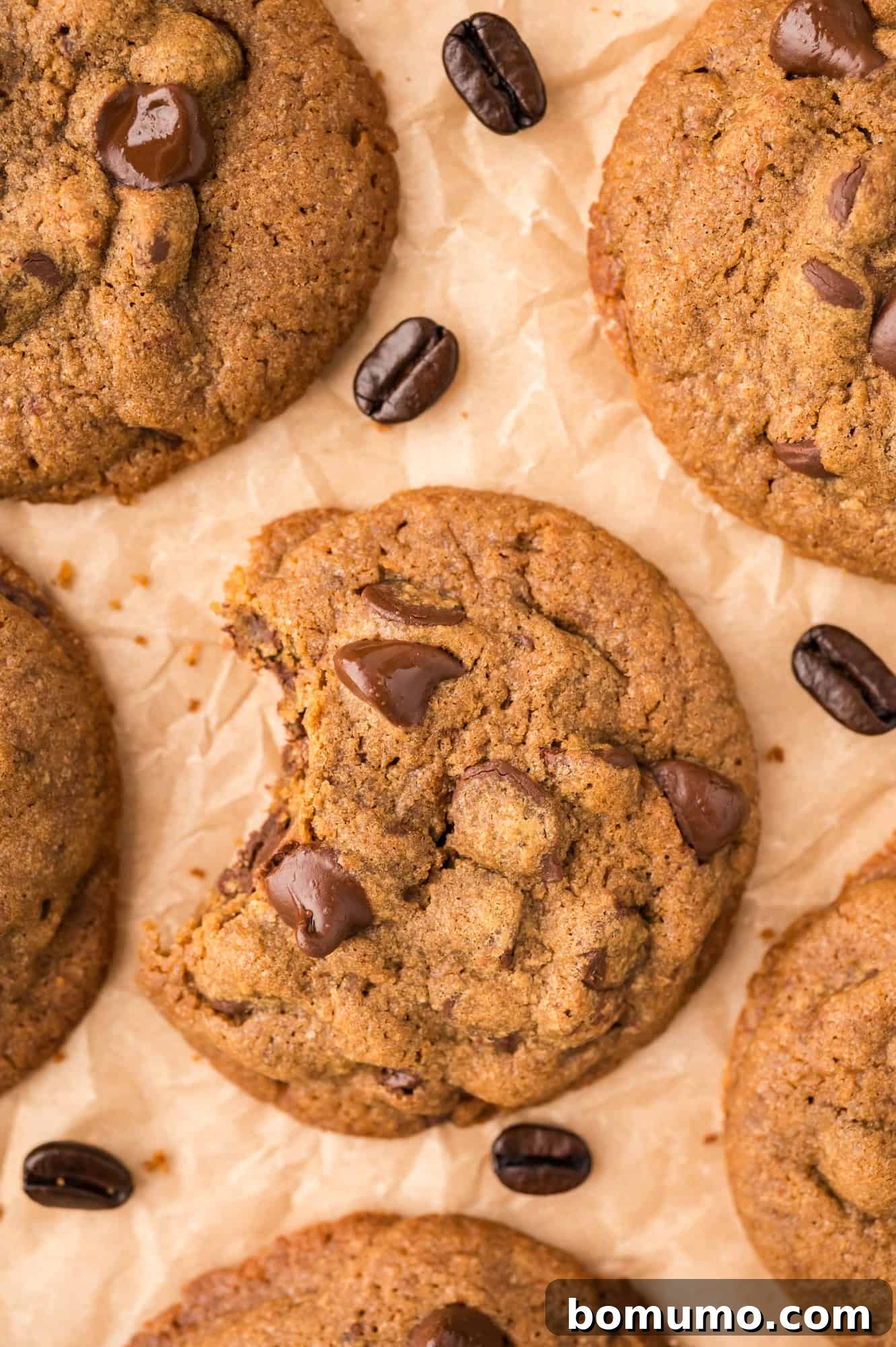 Several rich coffee cookies with visible chocolate chips, artfully arranged on brown parchment paper next to scattered coffee beans.