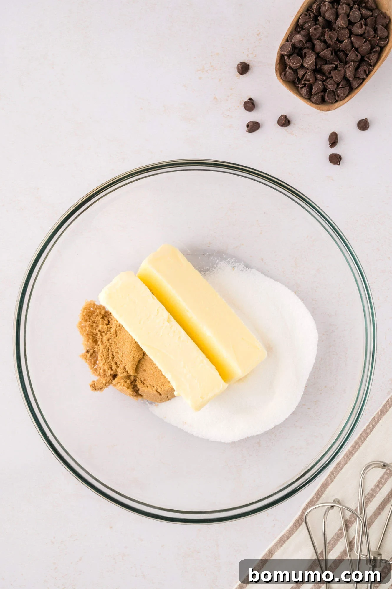 Softened butter and a blend of granulated and brown sugars in a clear glass mixing bowl, poised for creaming.