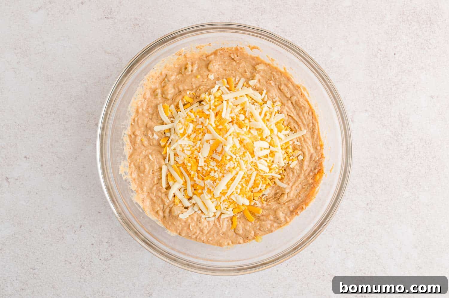 Smooth Bean Party Pleaser 8 Shredded cheese resting on top of the mixed bean dip, ready to be folded in.