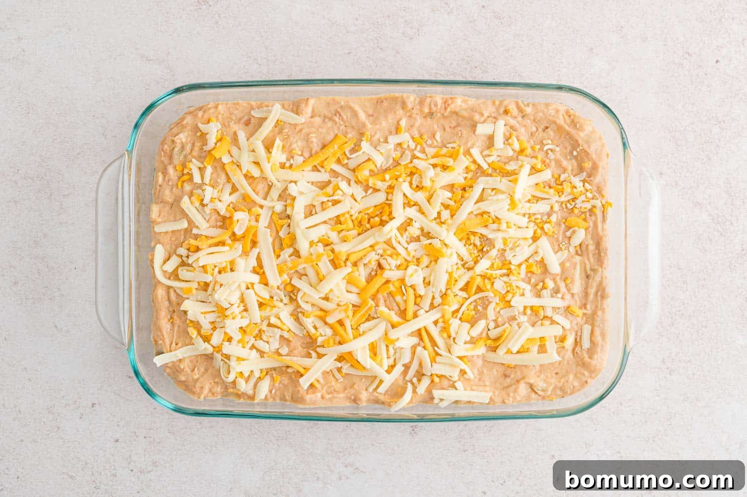 Smooth Bean Party Pleaser 10 Unbaked bean dip in a baking dish, topped with a generous layer of shredded cheese.