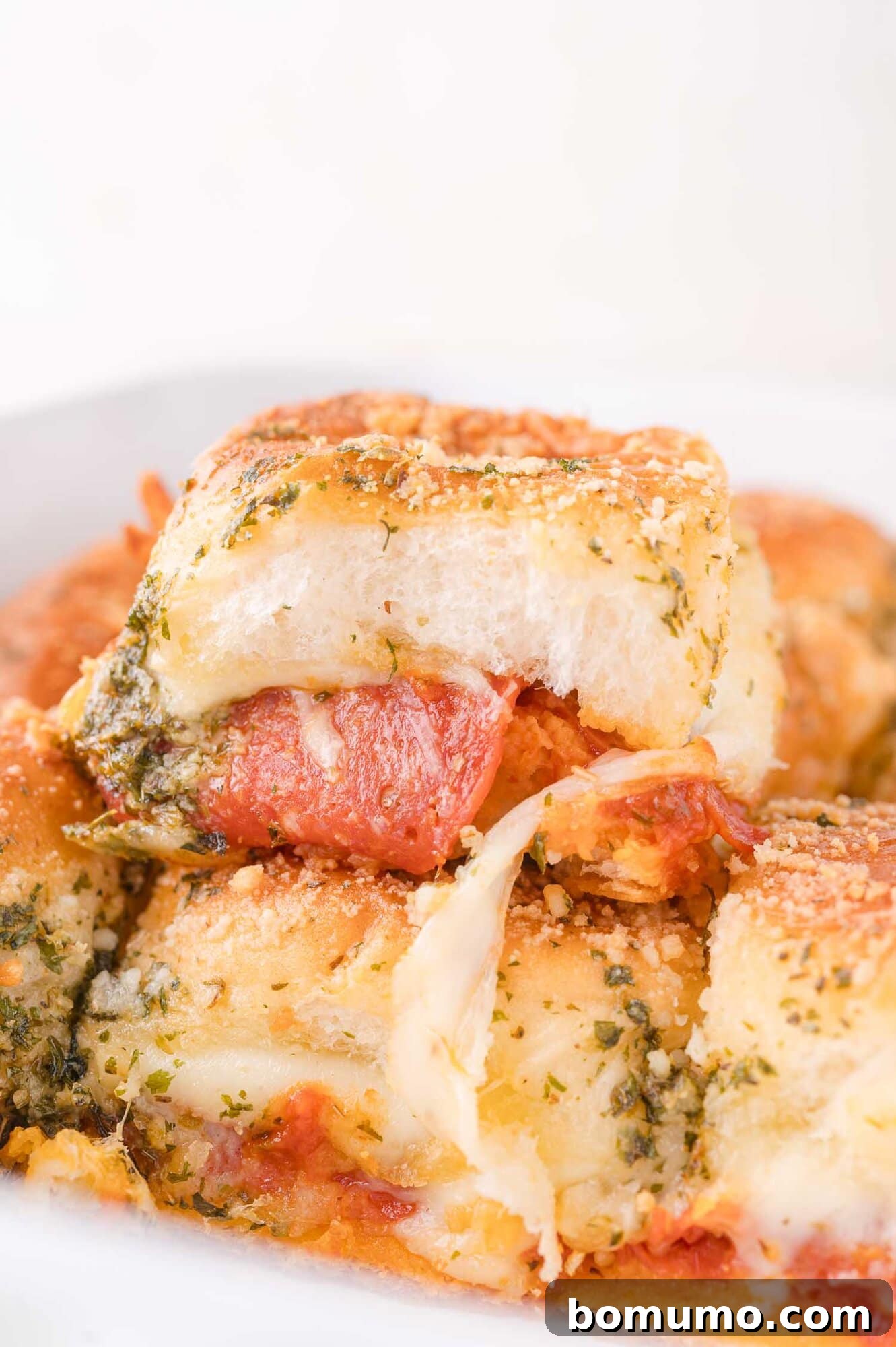 Gooey Pizza Pull-Aparts 2 A close-up of baked pizza slider filled with melted cheese and pepperoni, topped with herbs and grated parmesan.