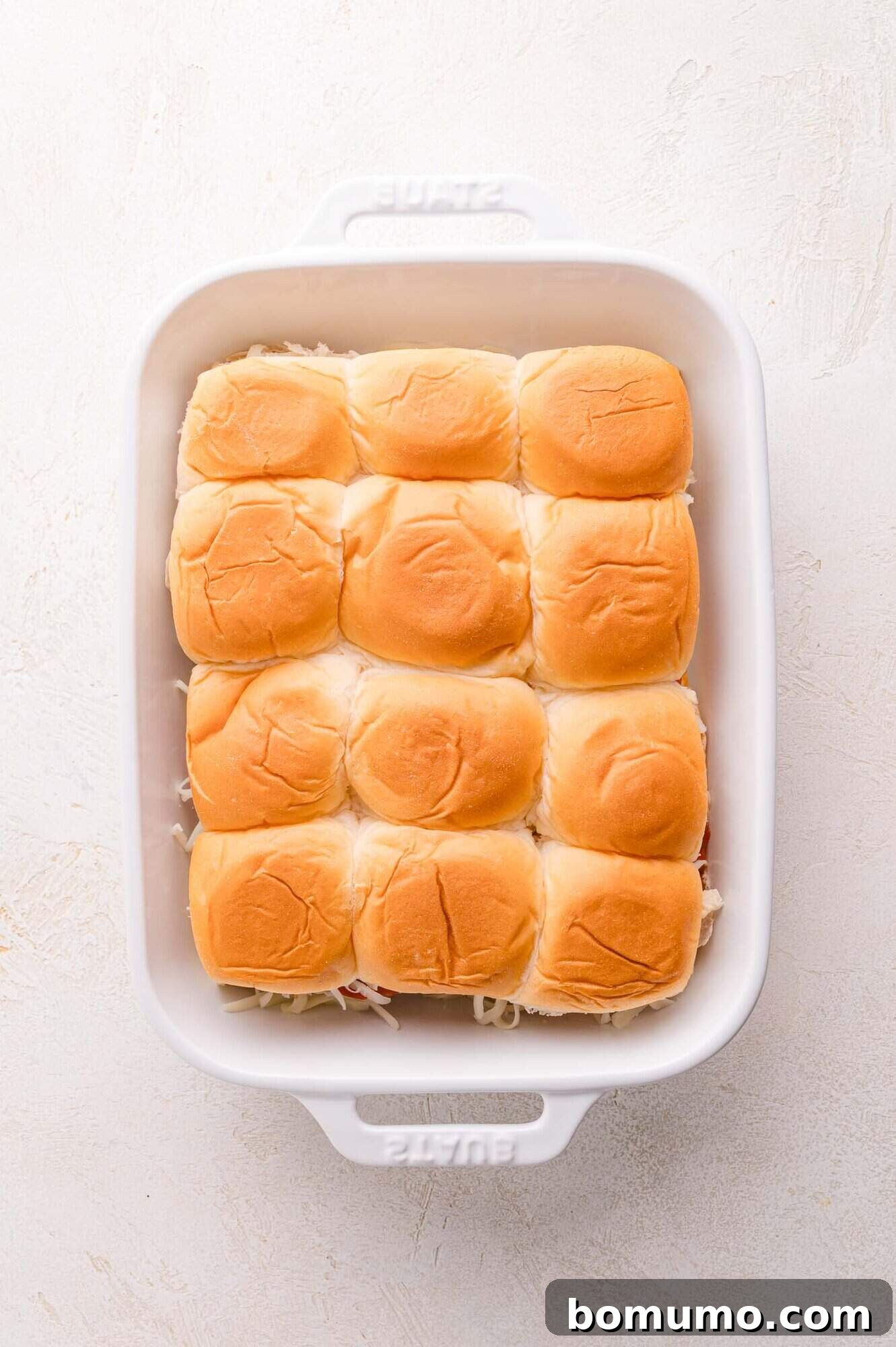Gooey Pizza Pull-Aparts 13 A white baking dish containing a single layer of twelve sandwich rolls arranged in three rows of four.