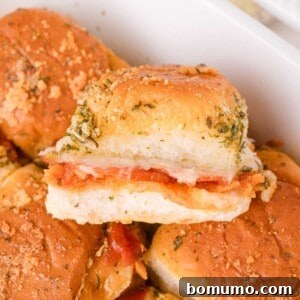 Close-up of a pizza slider sandwich filled with pepperoni and melted cheese, topped with herbs and grated cheese, in a white dish.