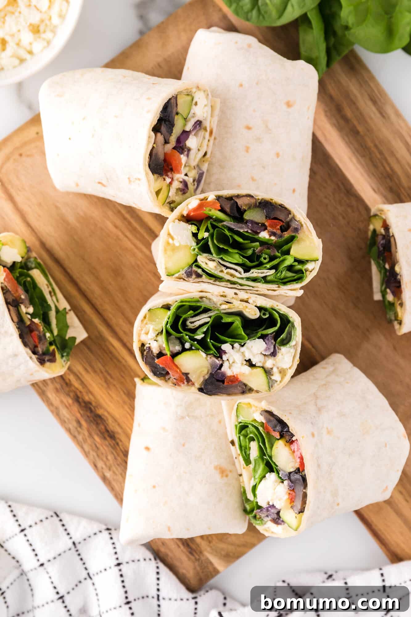 Assorted halves of perfectly rolled roasted vegetable wraps, showcasing their layers of fillings, neatly arranged on a wooden cutting board.