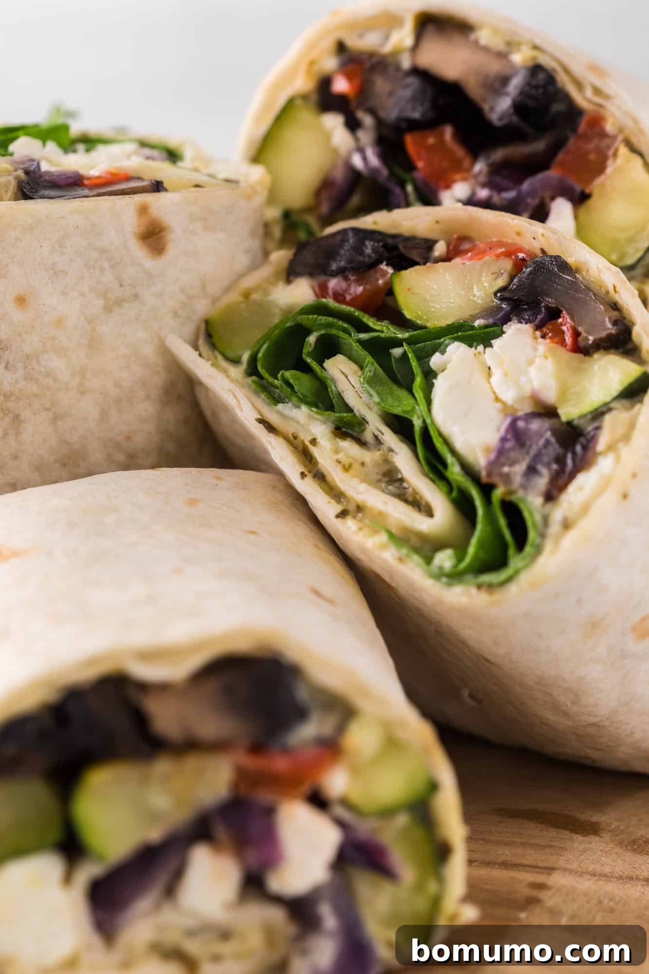 Close-up view of perfectly arranged roasted vegetable wraps, cut in half to showcase their richly textured fillings.