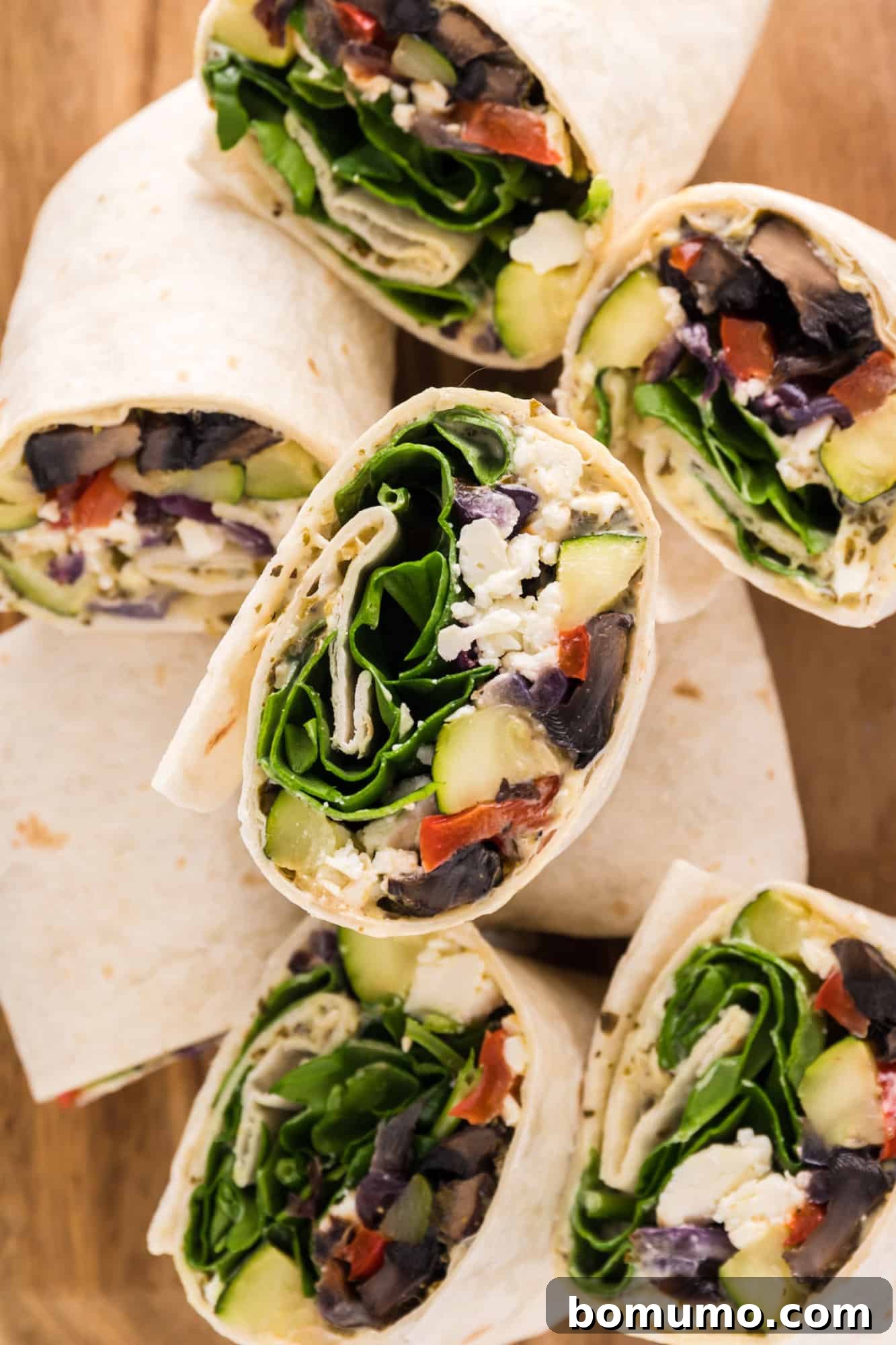 Assorted halves of freshly prepared roasted vegetable wraps artfully arranged on a rustic wooden cutting board, showcasing their vibrant fillings.