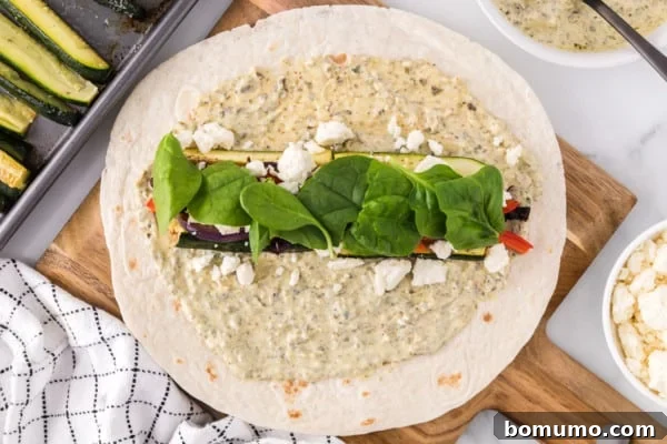 Fresh baby spinach leaves gracefully layered over a generous helping of roasted vegetables and crumbled feta, positioned in the center of a soft tortilla wrap.