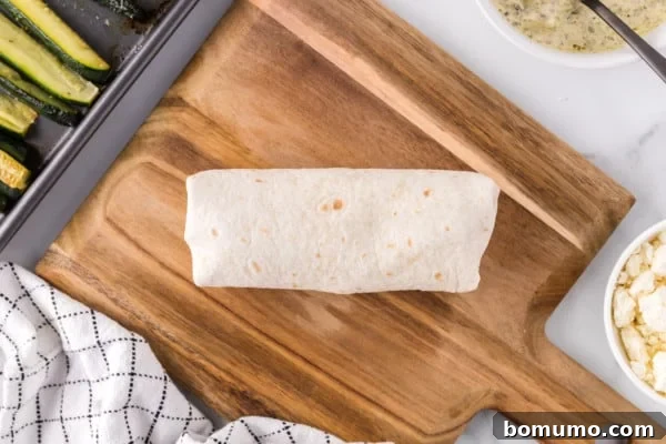 A perfectly rolled veggie wrap, firm and ready to eat, resting on a rustic wooden cutting board.