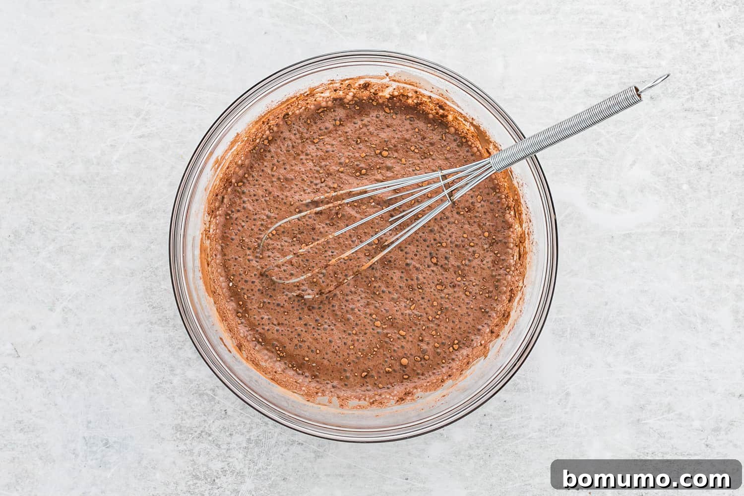 A whisk actively stirring the chocolate chia pudding ingredients in a glass bowl, showing the initial mixing process.