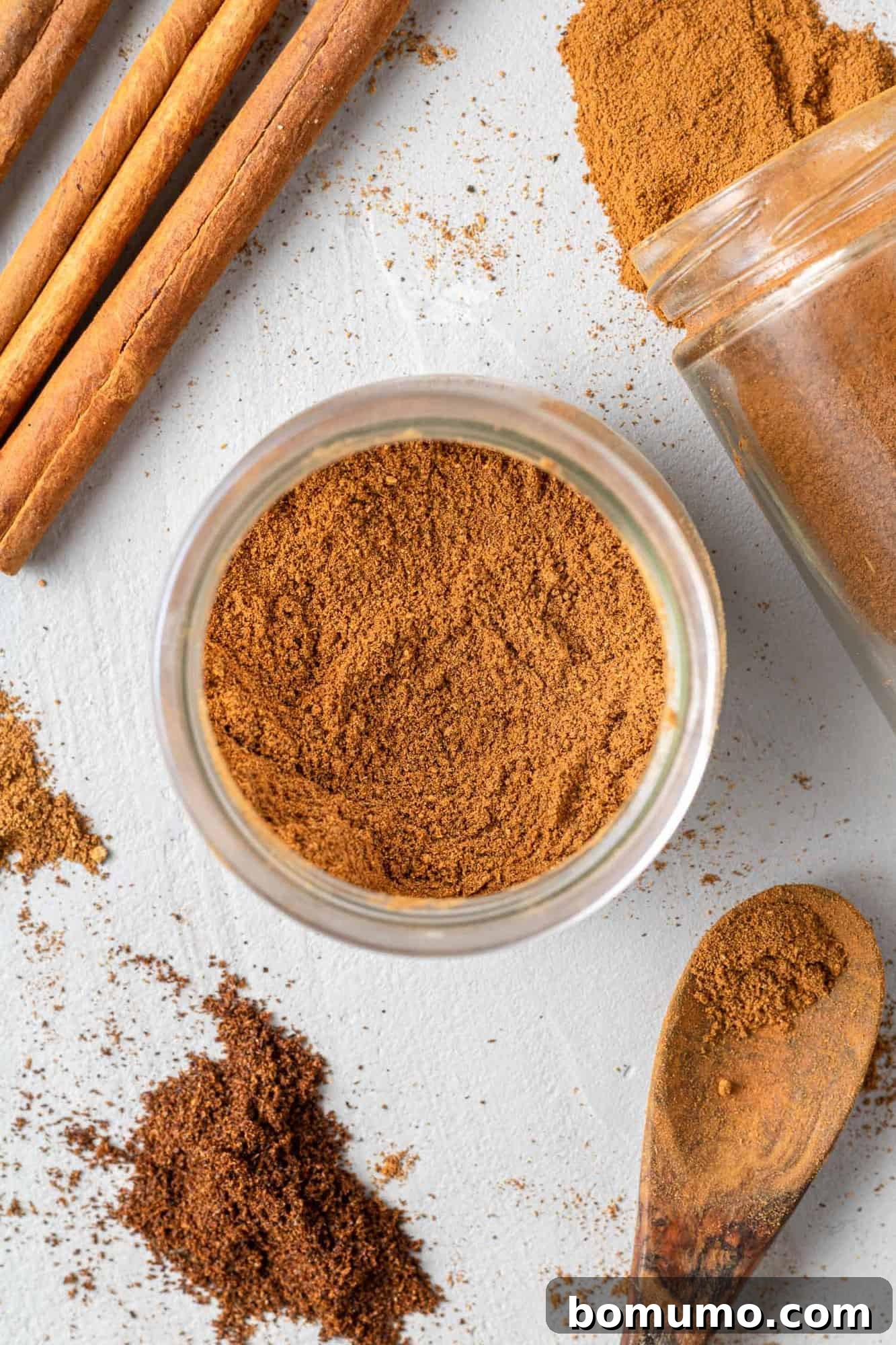 A charming overhead shot of a jar filled with freshly made homemade pumpkin spice, surrounded by whole cinnamon sticks, star anise, and fresh ginger, evoking a warm, autumnal feeling.