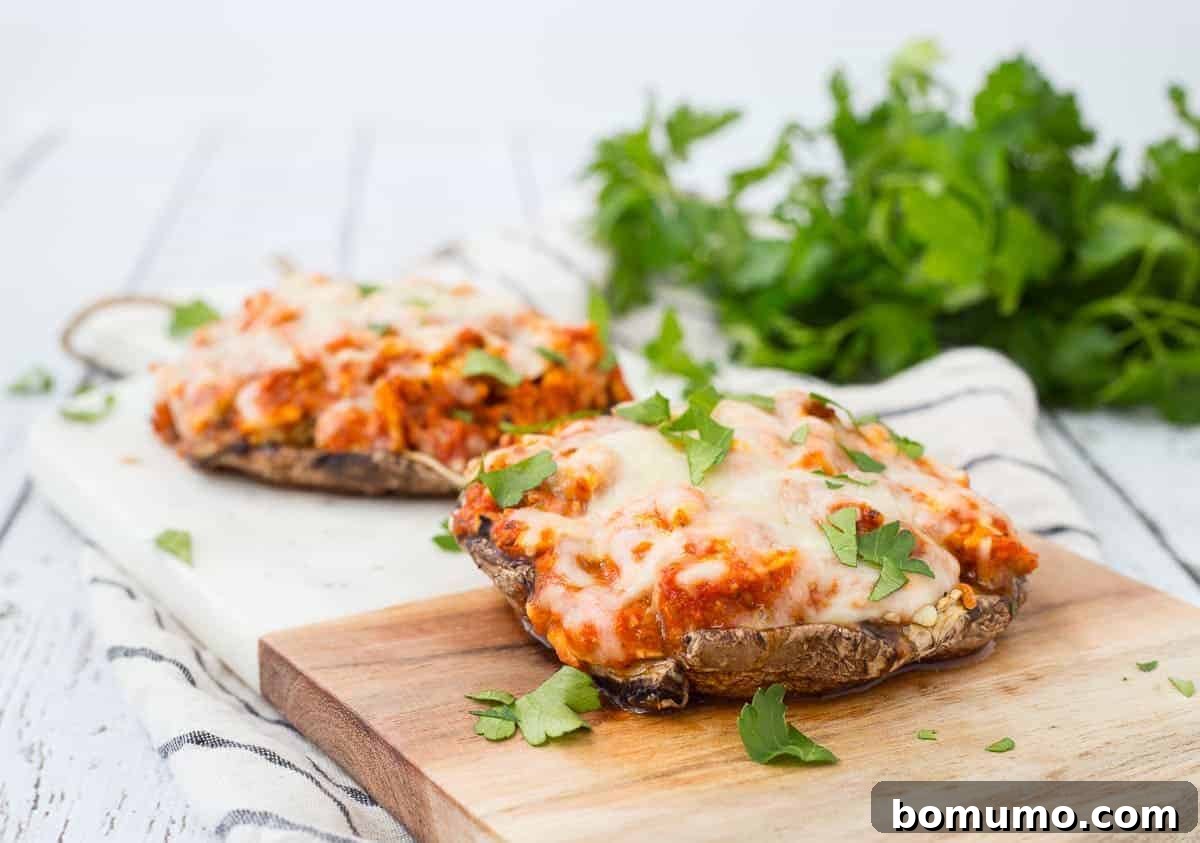 Front view of golden-brown chicken Parmesan stuffed mushrooms on a cutting board, garnished lightly.