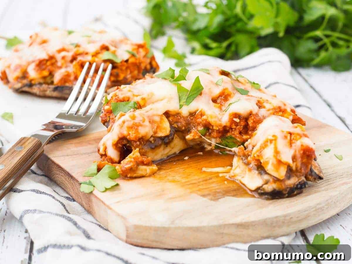 A stuffed portobello mushroom on a board, with a portion removed to show the filling, a fork resting alongside.