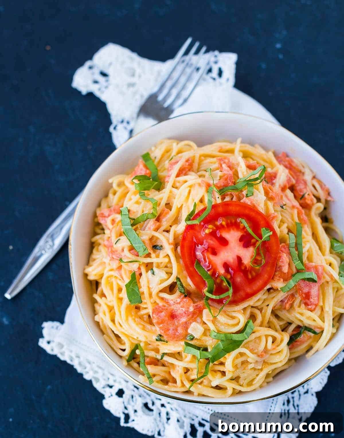Overhead image of angel hair pasta with a tomato cream sauce, garnished with fresh basil and a tomato slice.
