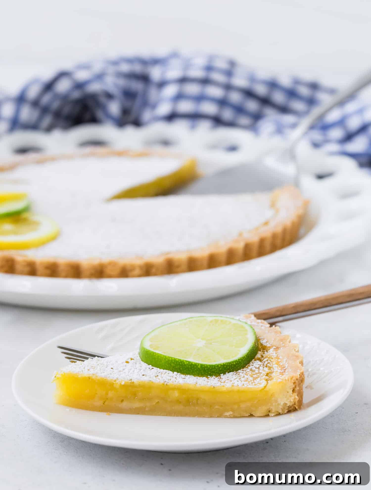 A perfectly sliced lemon lime tart, revealing its creamy, bright yellow filling and the crisp, golden-brown shortbread crust.