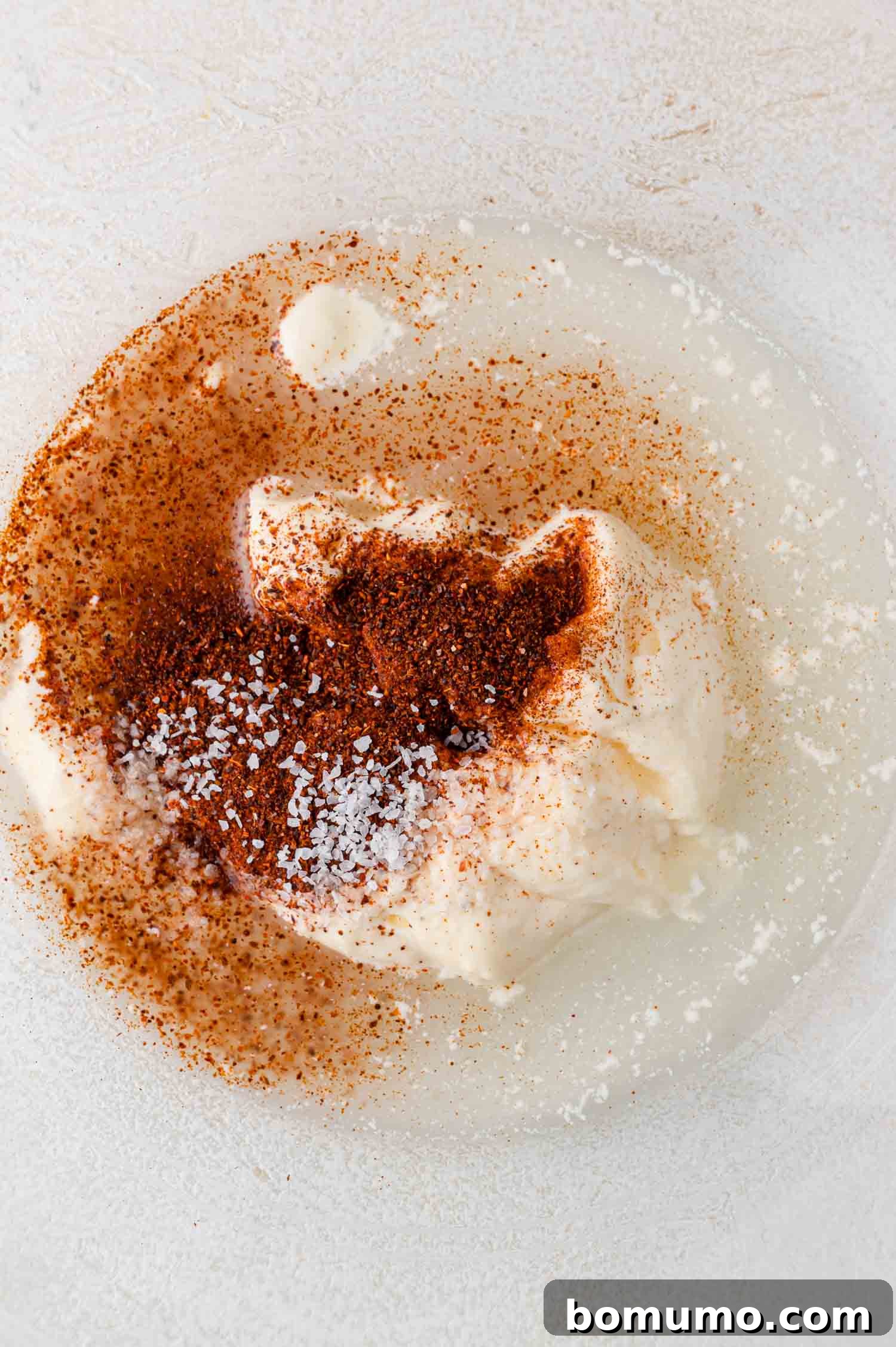 A white plate with mayonnaise, chili powder, salt, and lime juice mixed together, ready for whisking.