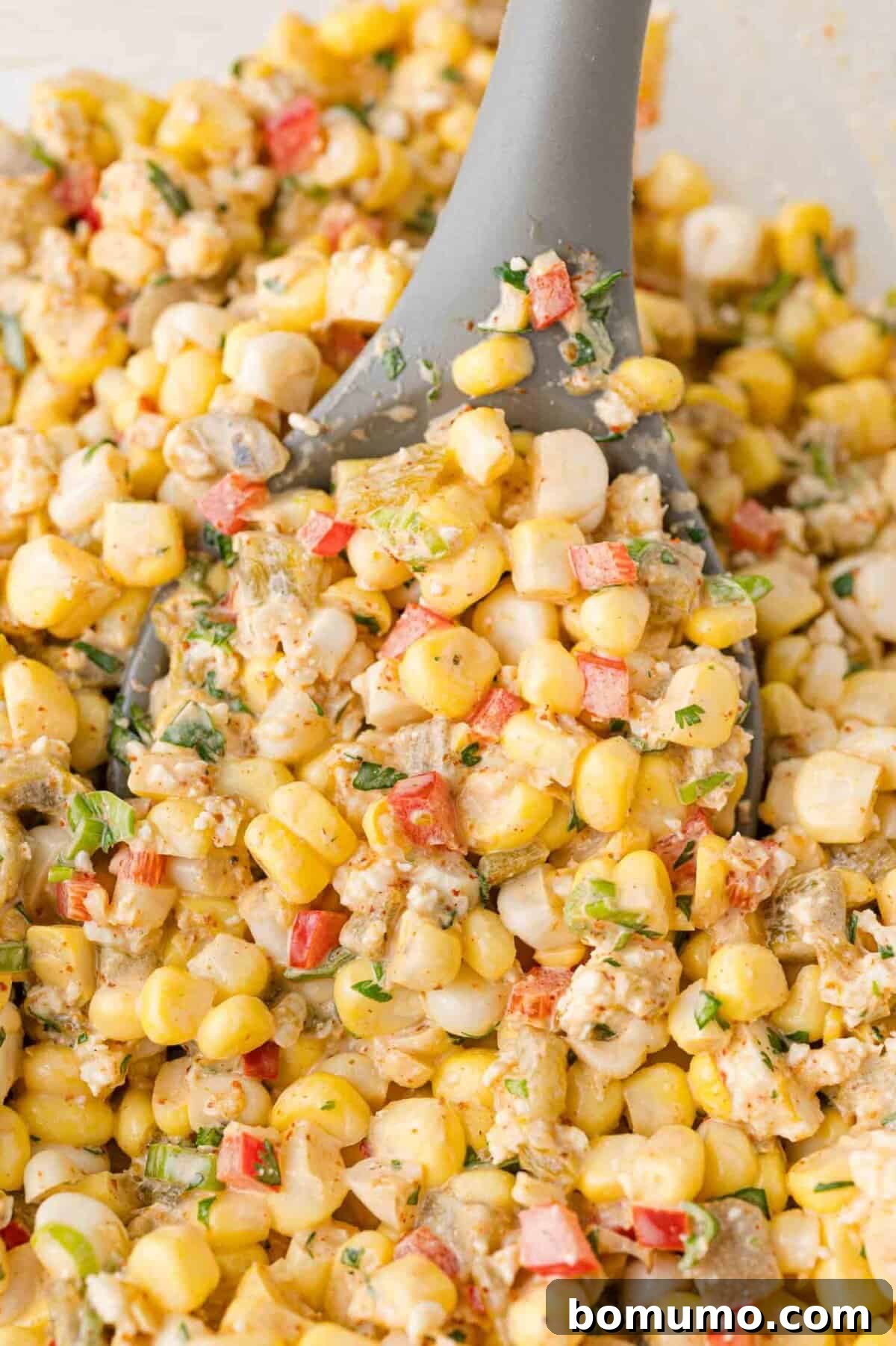 Close-up of a creamy and flavorful corn dip with a gray serving spoon, showcasing its texture and ready-to-eat appeal.
