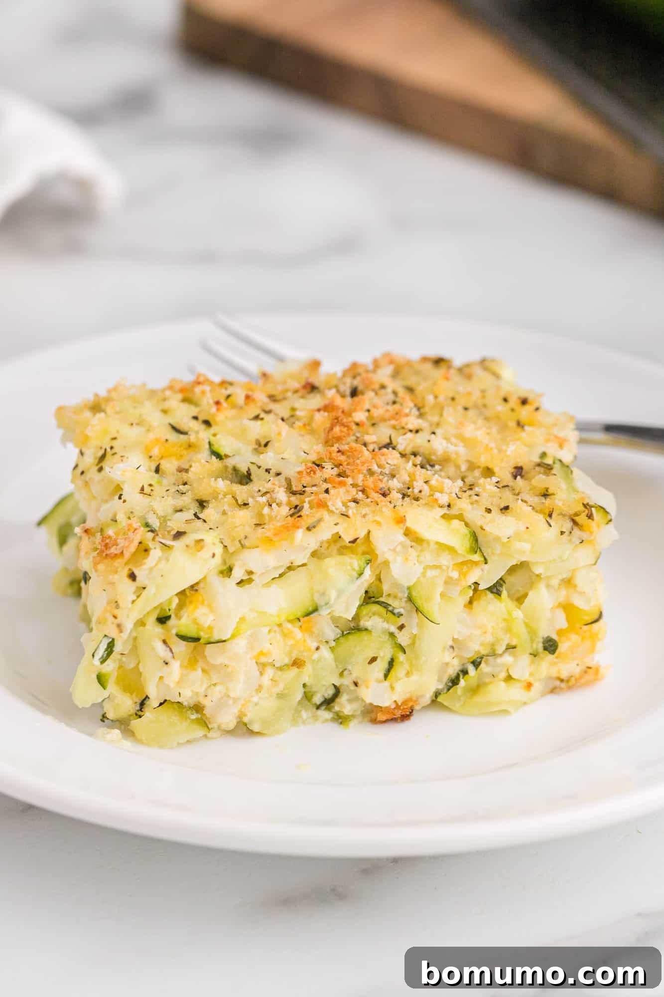 A golden-brown slice of cheesy zucchini and rice casserole with a crispy topping, served on a white plate, highlighting its comforting texture.