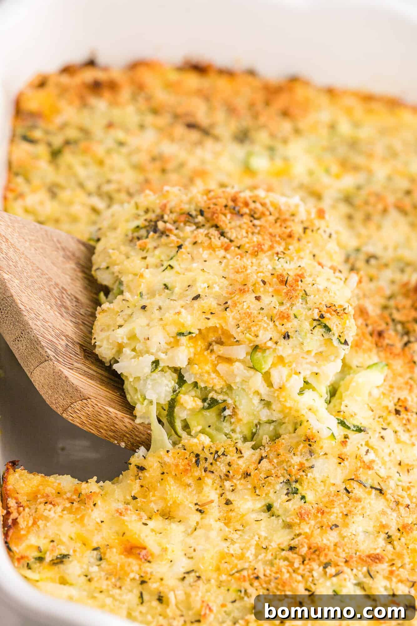 A serving of the golden-brown zucchini casserole being scooped from the baking dish, revealing its warm, cheesy interior.