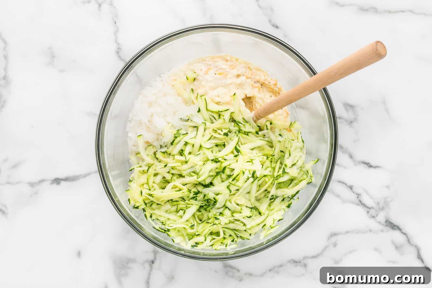 All the zucchini casserole ingredients, including shredded zucchini, rice, and onions, combined in a large mixing bowl, ready for baking.