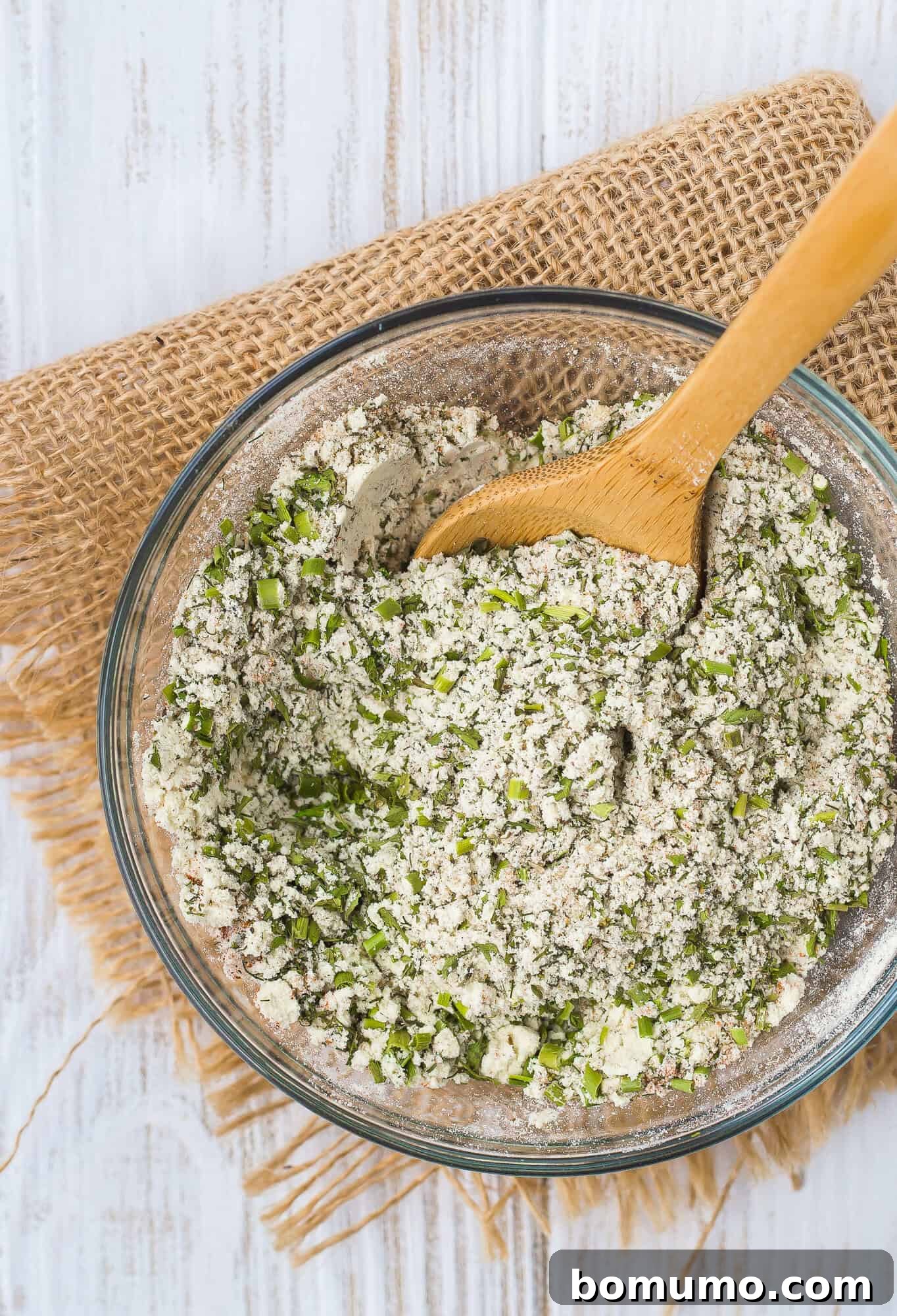 A small jar of homemade ranch seasoning mix with a wooden spoon beside it, suggesting culinary use.