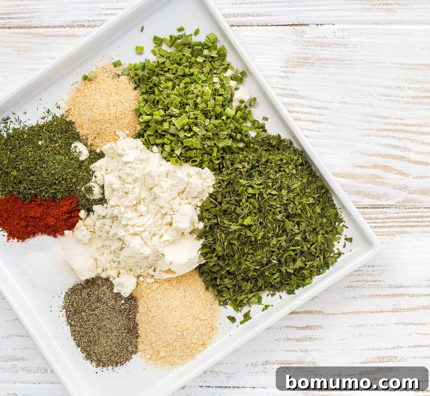 Individual ingredients for ranch seasoning mix artfully arranged on a white plate, showcasing their freshness.