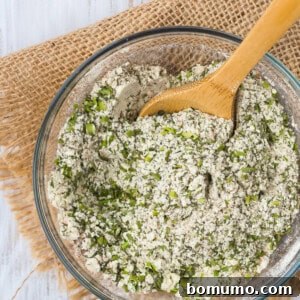 A small jar of homemade ranch seasoning mix with a wooden spoon beside it.