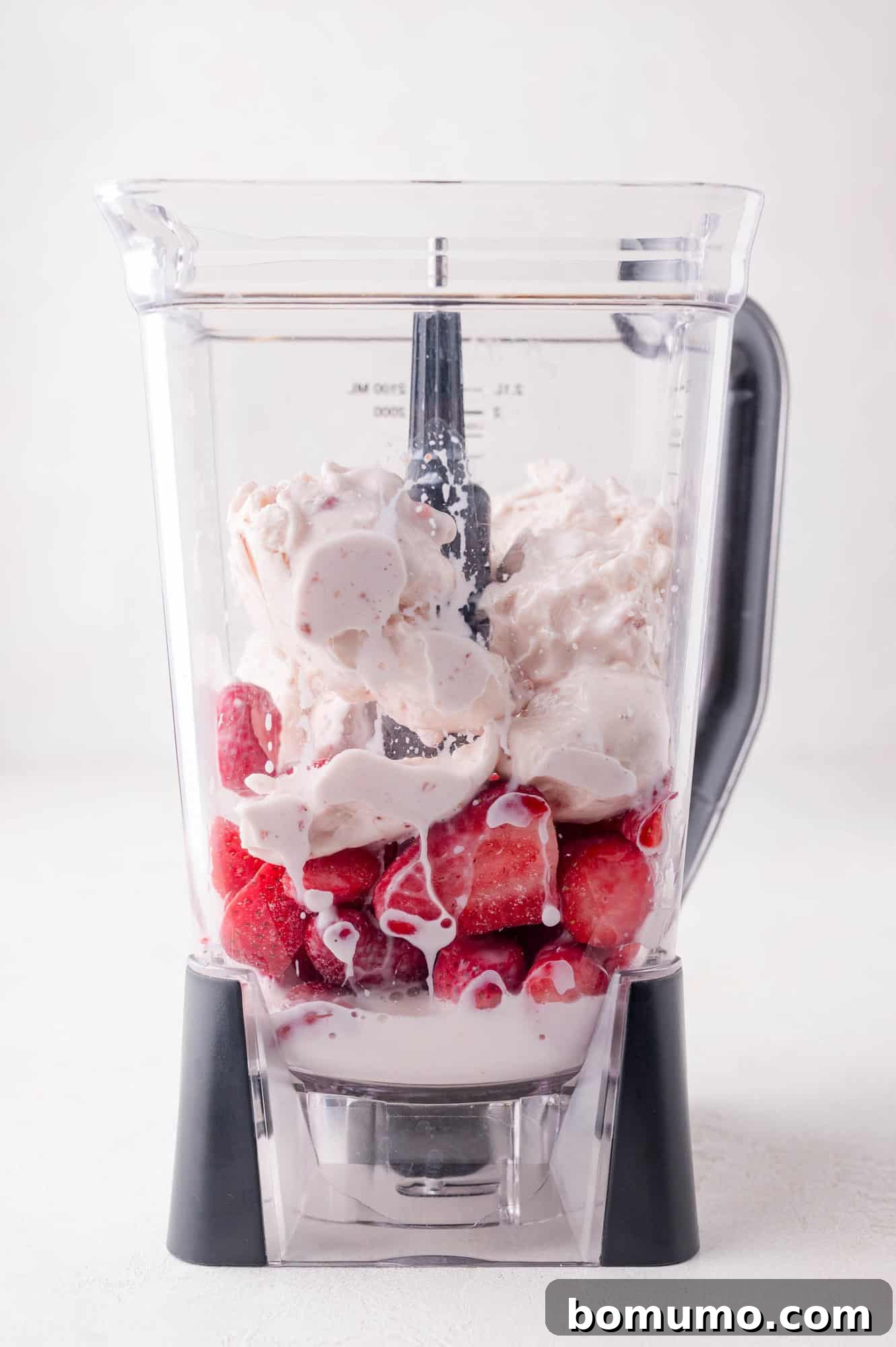 Velvet Strawberry Indulgence 4 A blender ready for action, filled with the core ingredients for a strawberry milkshake: a generous amount of frozen strawberries, dollops of creamy vanilla ice cream, and a small pool of milk at the base, awaiting transformation.
