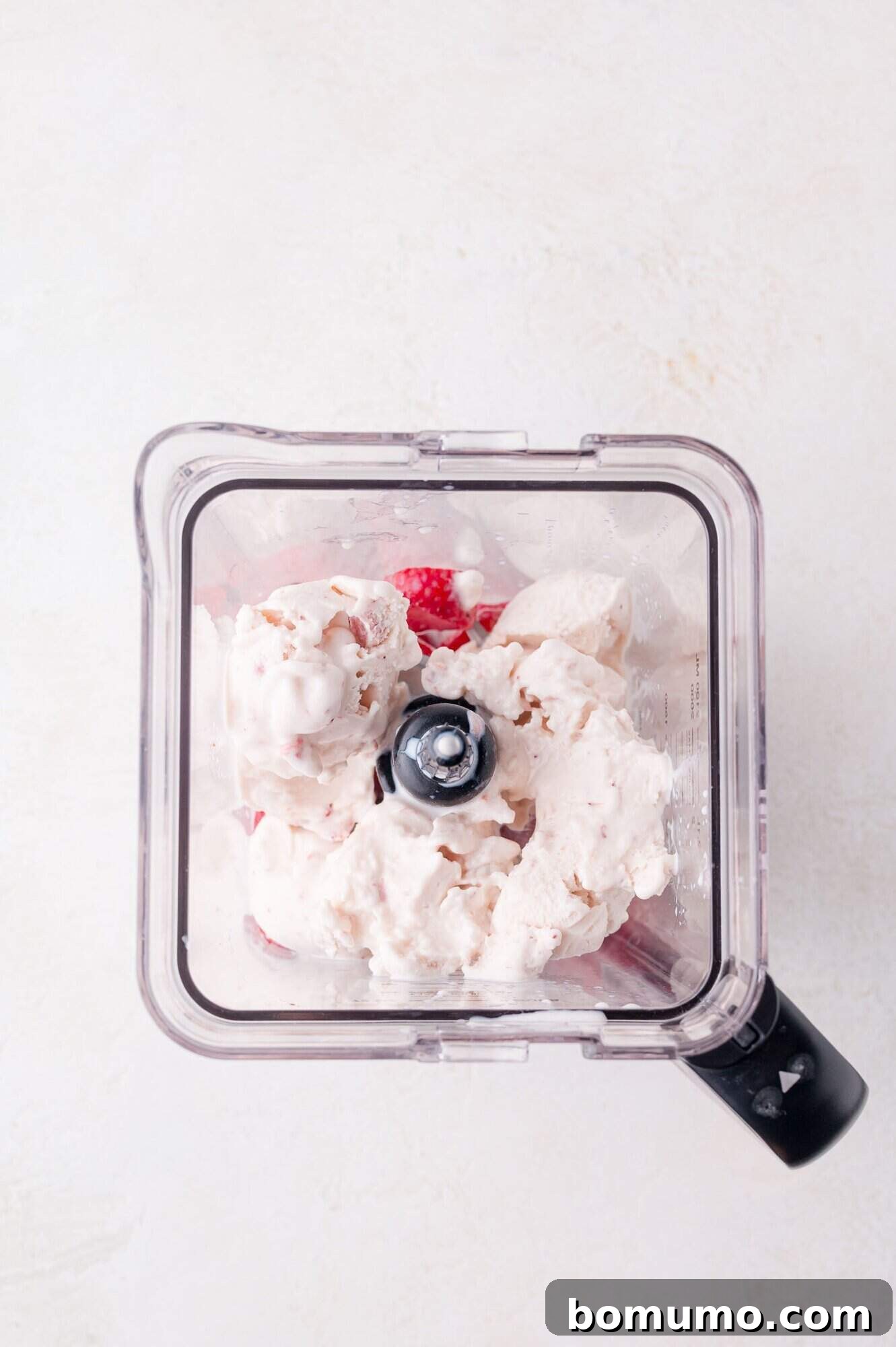Velvet Strawberry Indulgence 5 A top-down, close-up view of a blender canister, showcasing a luscious blend of ice cream and strawberries, halfway through the blending process, promising a creamy and refreshing strawberry milkshake.