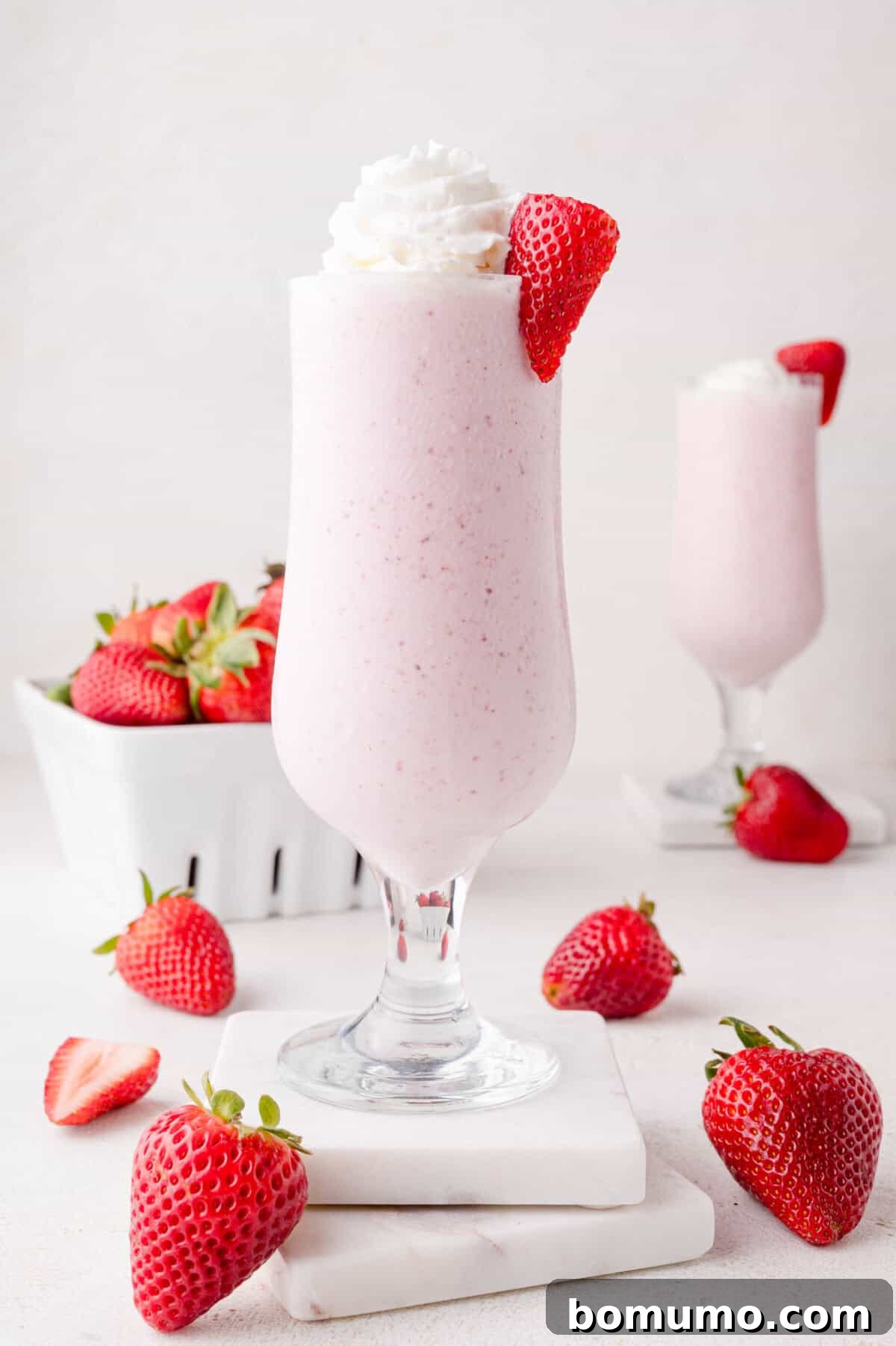 Velvet Strawberry Indulgence 8 A tall, inviting glass of homemade strawberry milkshake crowned with a generous dollop of whipped cream and a single fresh strawberry. The glass sits on a pristine white surface, surrounded by more vibrant fresh strawberries, creating a picture of ultimate summer refreshment.