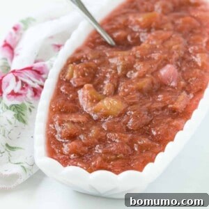 Light red rhubarb sauce in an oval shaped white bowl, ready to be served.