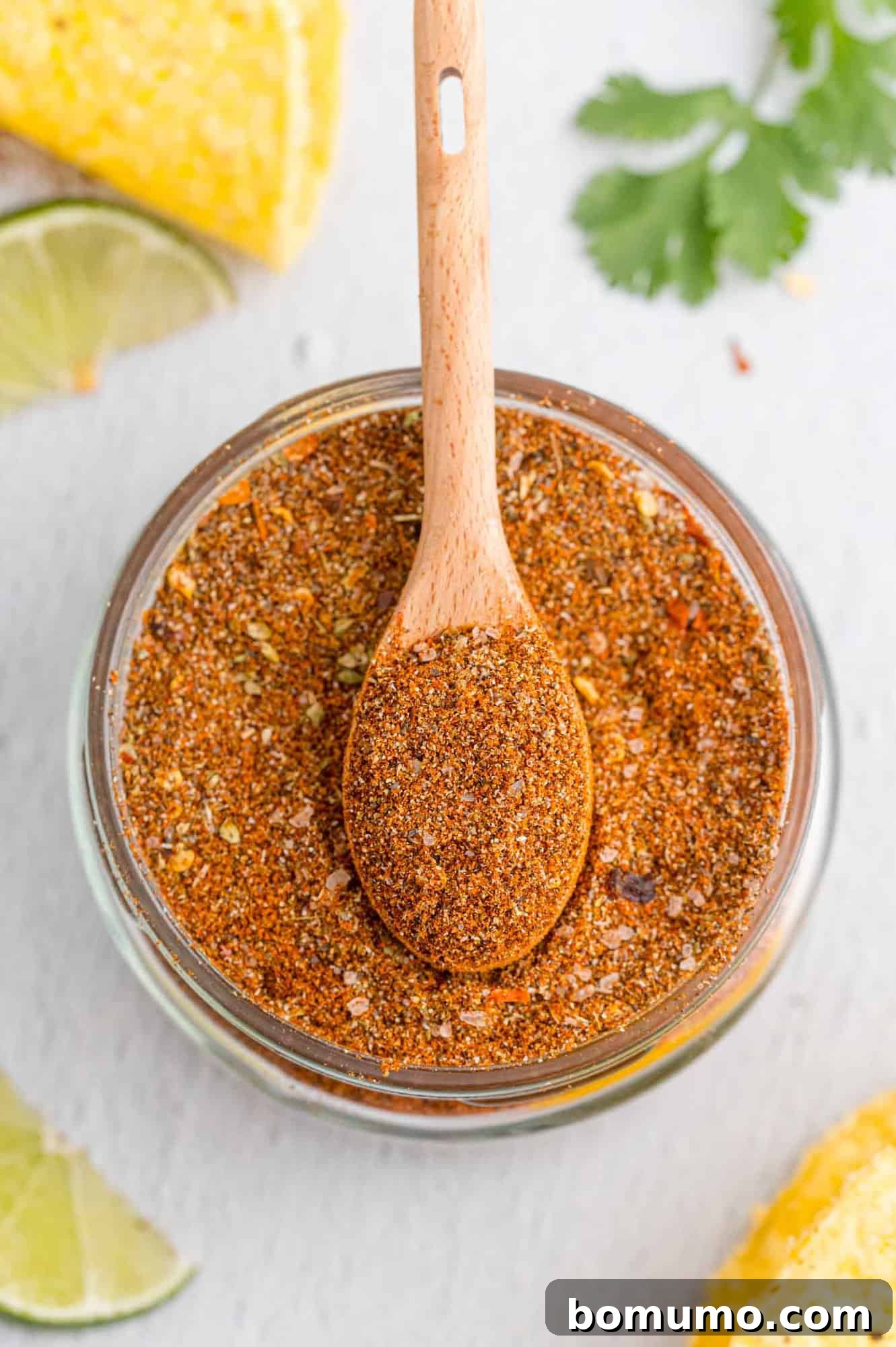 Overhead view of seasoning for tacos in a small glass jar with a wooden spoon.