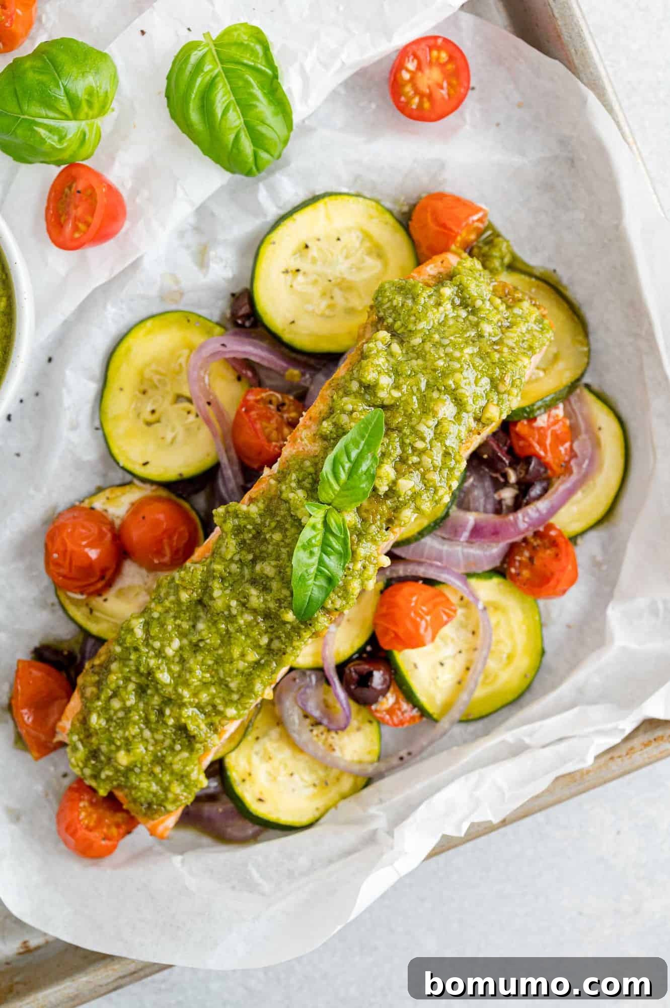 Overhead view of pesto salmon in parchment paper with vibrant vegetables, perfectly cooked and ready to serve.