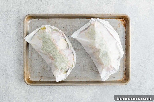 Two neatly sealed pesto salmon packets arranged on a rimmed baking sheet, prepared for the oven.