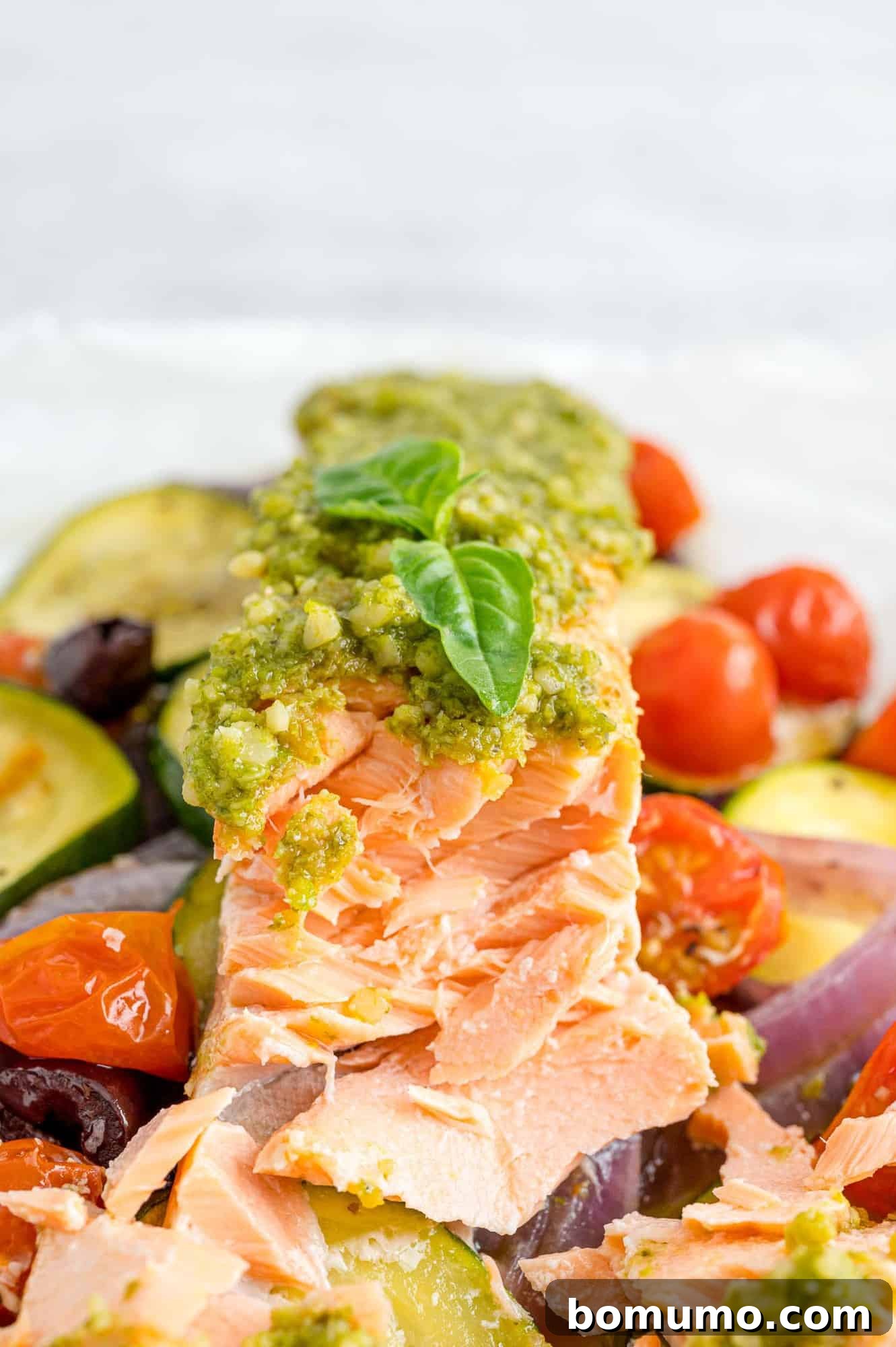 Pesto salmon on a bed of vegetables, expertly flaked to demonstrate its tender, moist texture.
