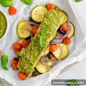 Vegetables and salmon topped with pesto in a parchment paper packet, forming a delicious and healthy meal.