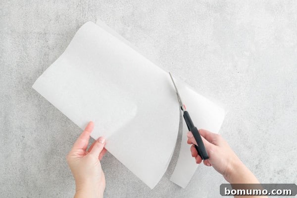 One hand holding folded parchment paper while the other hand uses scissors to cut out a half-oval.