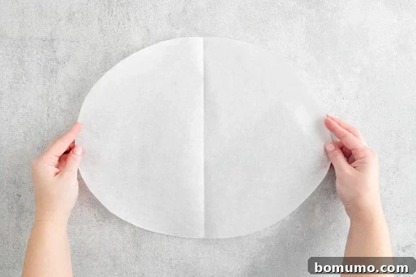 Two hands holding an unfolded parchment paper oval, ready for ingredients.