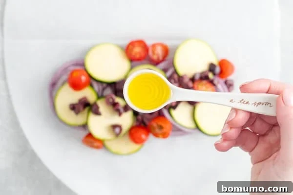 A spoonful of olive oil delicately drizzled over fresh vegetables arranged on a parchment paper oval.