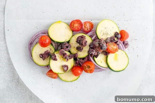 Chopped fresh vegetables, including zucchini, tomatoes, and red onion, neatly arranged over a parchment paper oval.