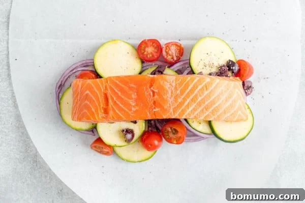 A succulent salmon fillet placed over a bed of colorful vegetables on a parchment paper oval, forming the base of the dish.