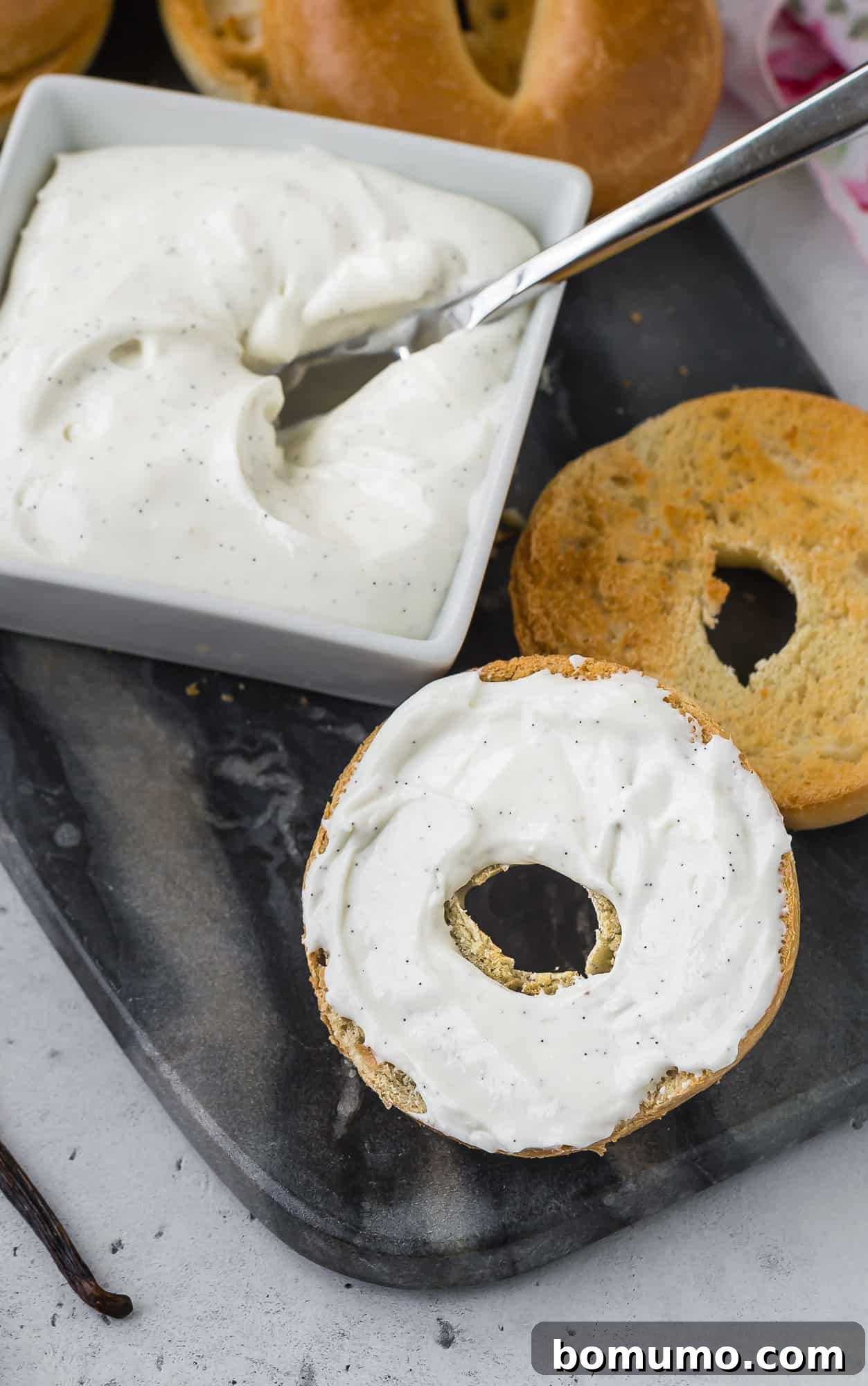 Knife spreading cream cheese on a bagel, with other bagels in the background.