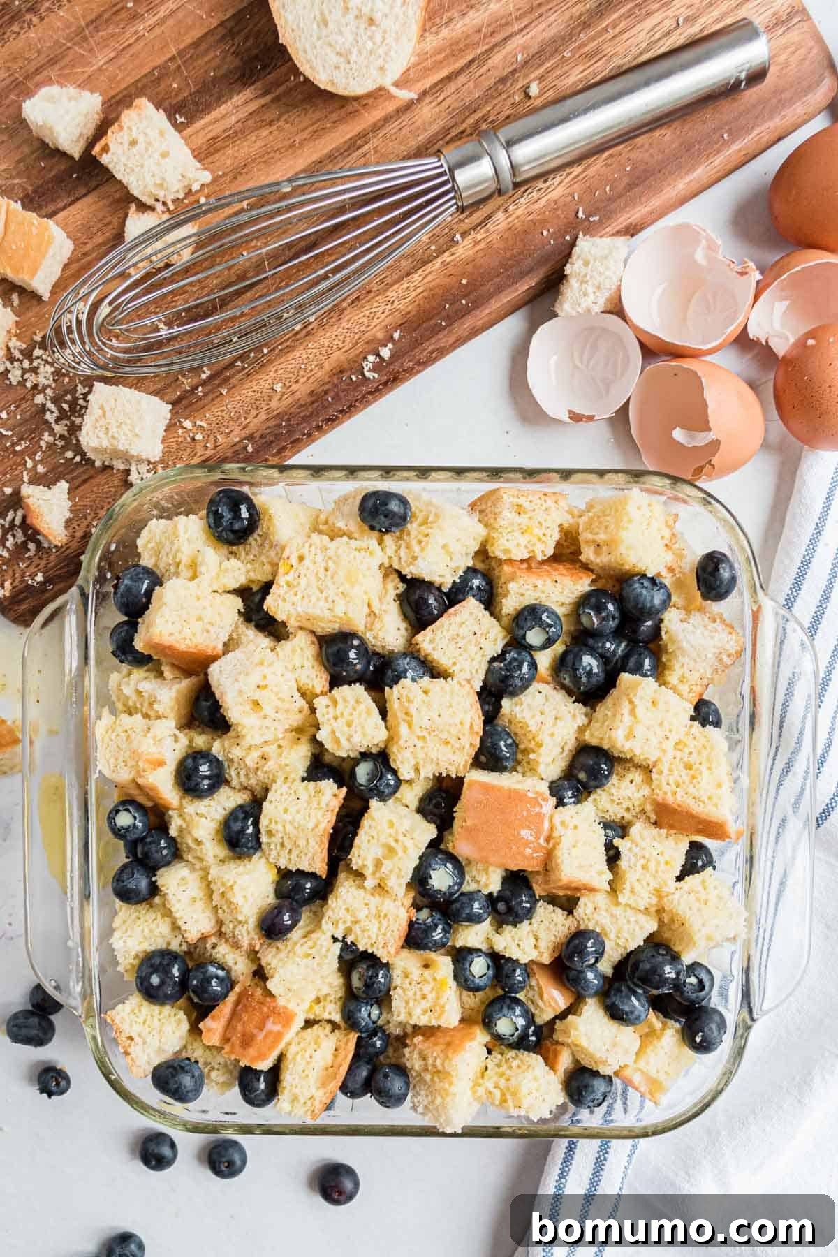 Comforting Blueberry Bread Pudding 4 A top-down view of cubed bread and plump blueberries arranged neatly in a greased baking dish, awaiting the custard mixture.