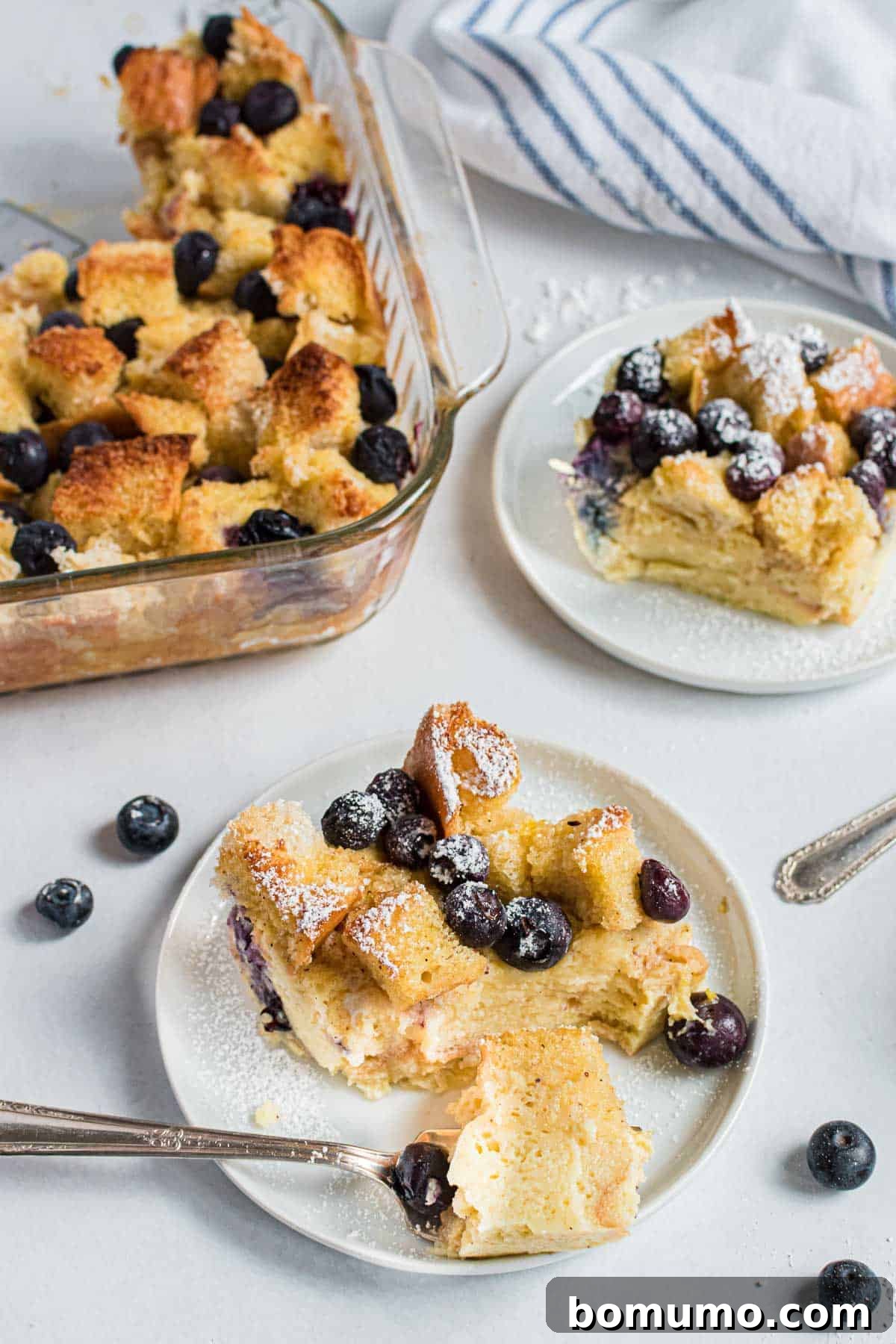Comforting Blueberry Bread Pudding 8 A fork is poised to take a piece of warm blueberry bread pudding from a plate, revealing its soft, custardy texture and juicy berries.