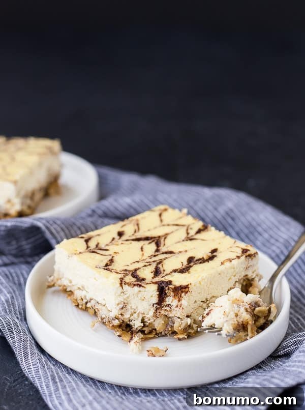 A perfectly portioned square slice of cinnamon swirl breakfast cheesecake on a round white plate, resting on a blue striped cloth. The cheesecake has a visible cinnamon swirl on top and a hearty oat crust.