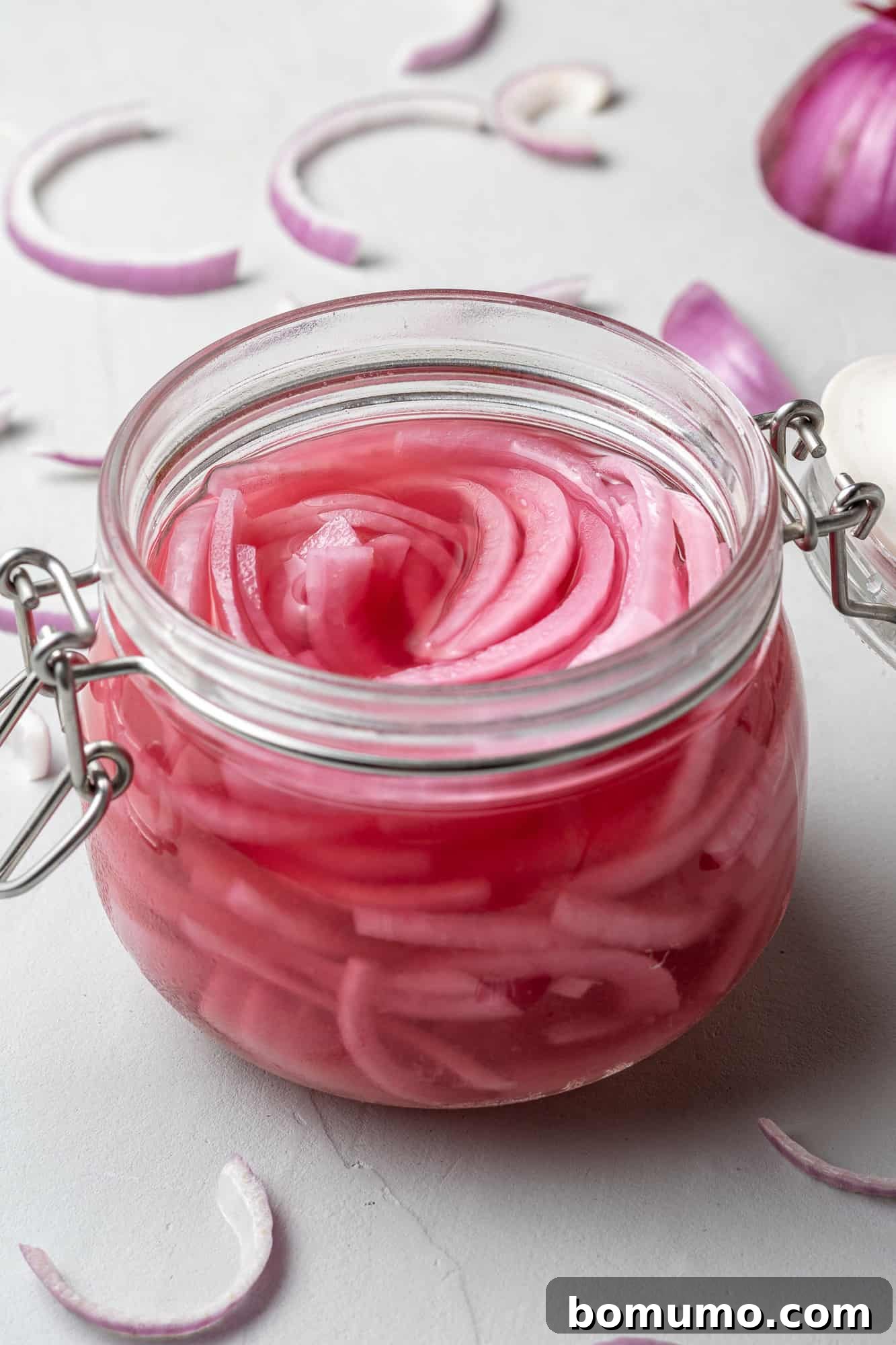 Pickled red onions in a small clear glass jar, showcasing their vibrant pink color.