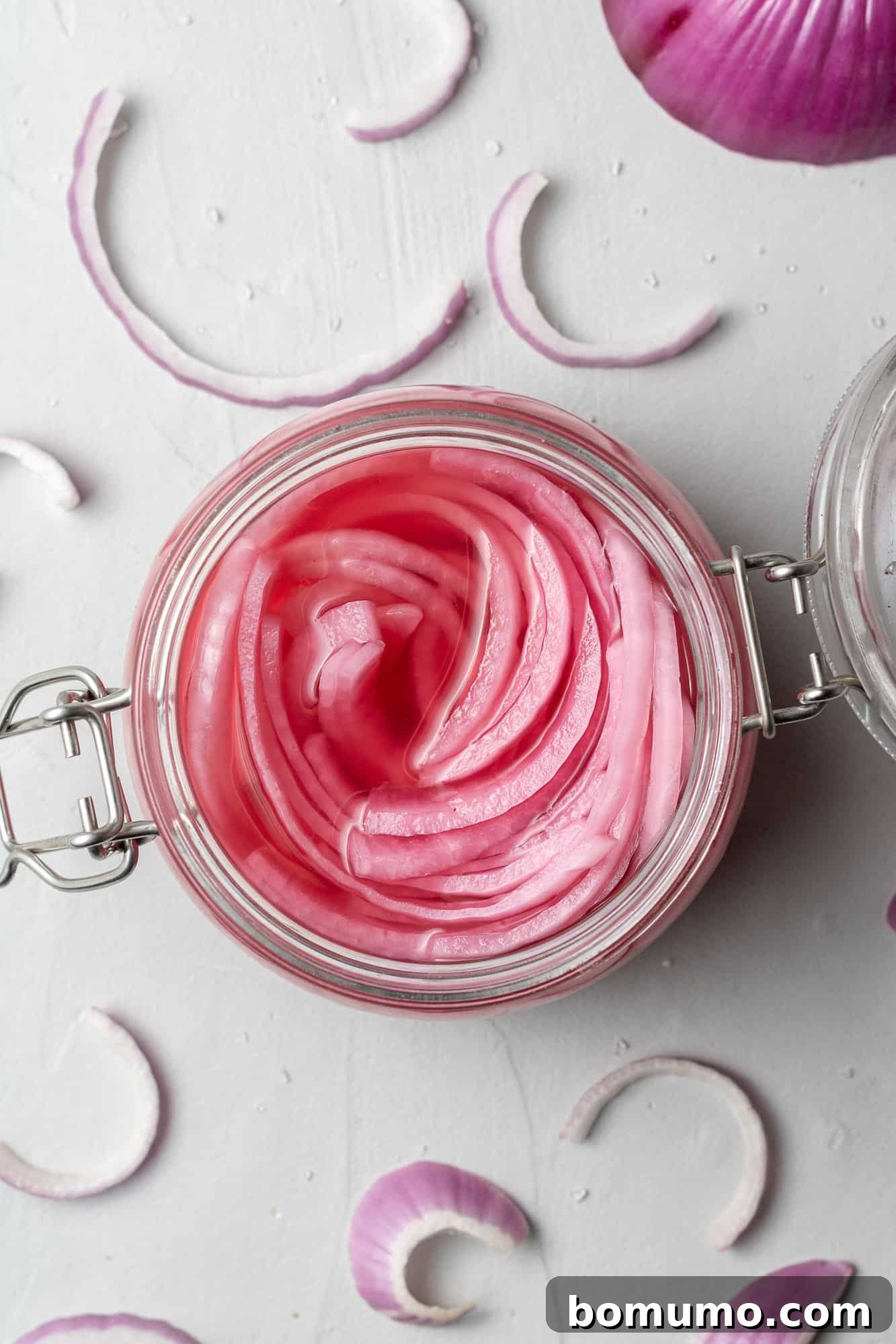 Overhead view of a clear glass jar filled with vibrant pickled red onions.