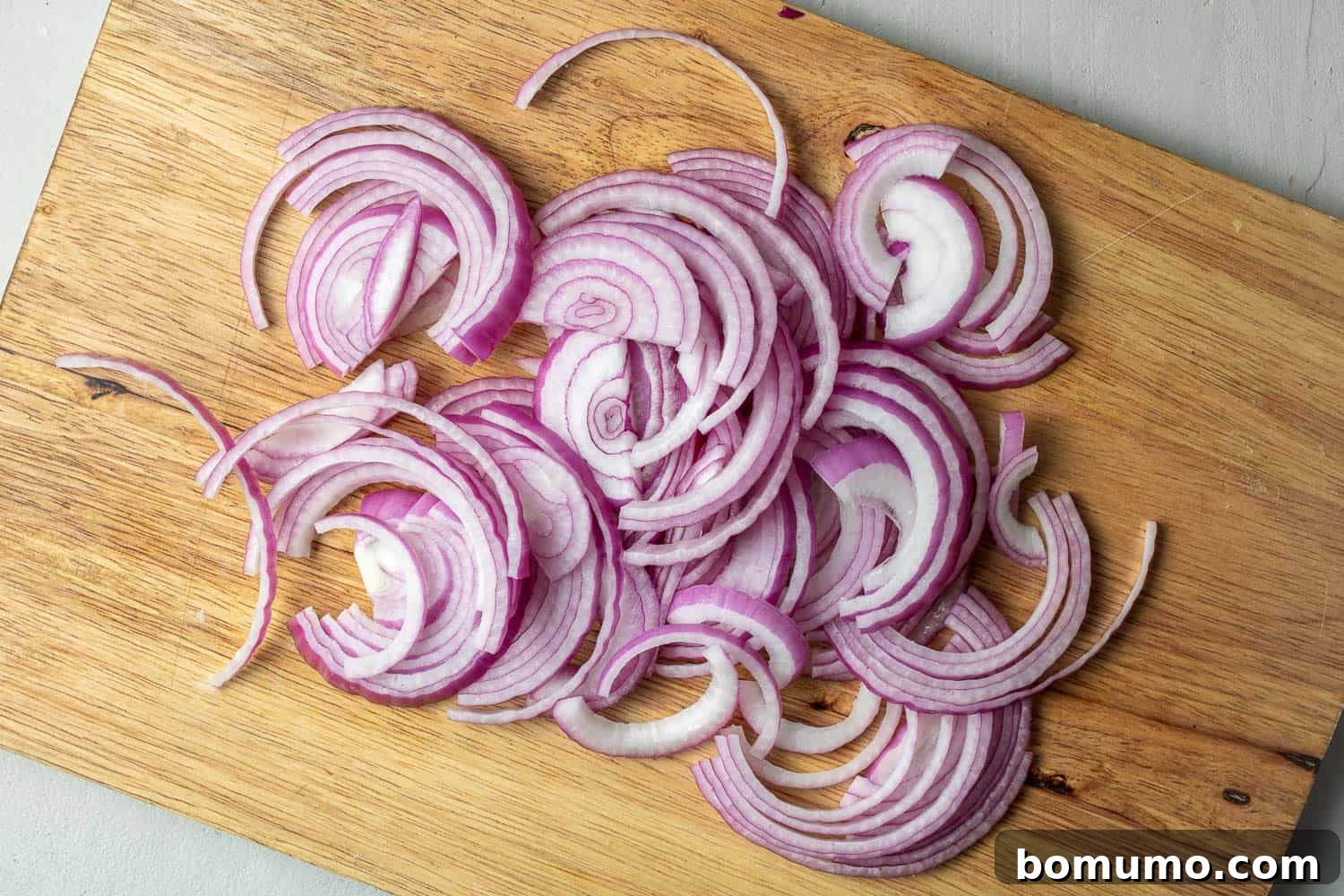 Thinly sliced red onions arranged on a rustic wooden cutting board.