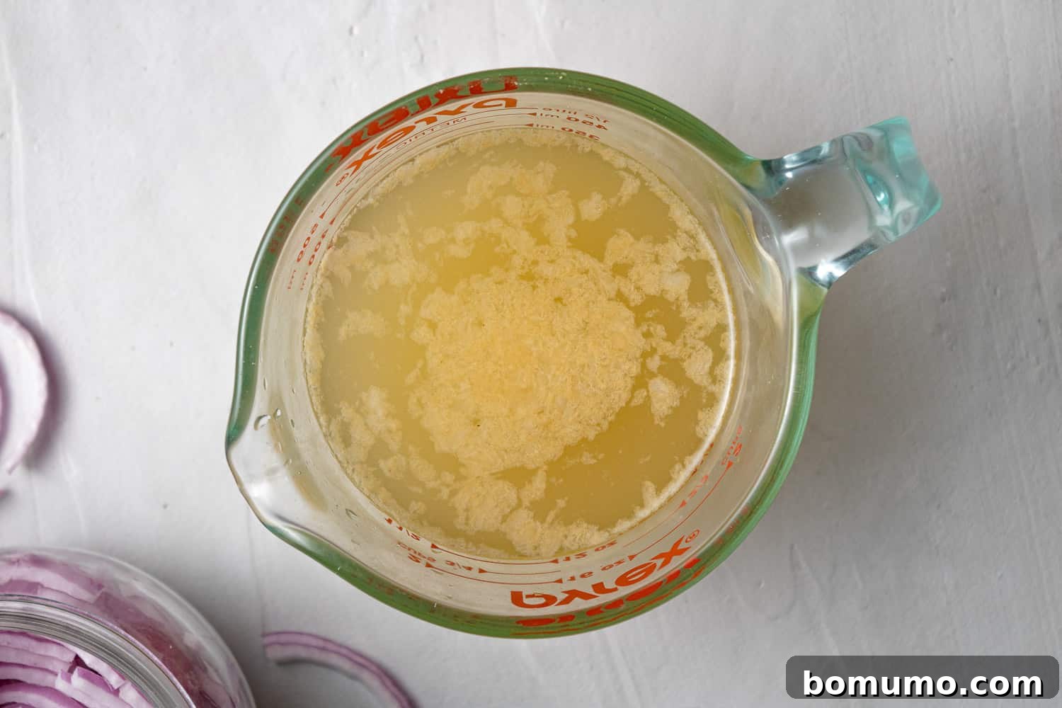 Clear glass measuring cup containing the pickling liquid: a mixture of vinegar, warm water, sugar, and salt.