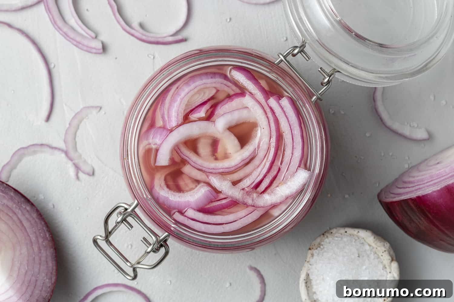 Sliced red onions fully immersed in clear pickling brine within a glass jar, viewed from above.