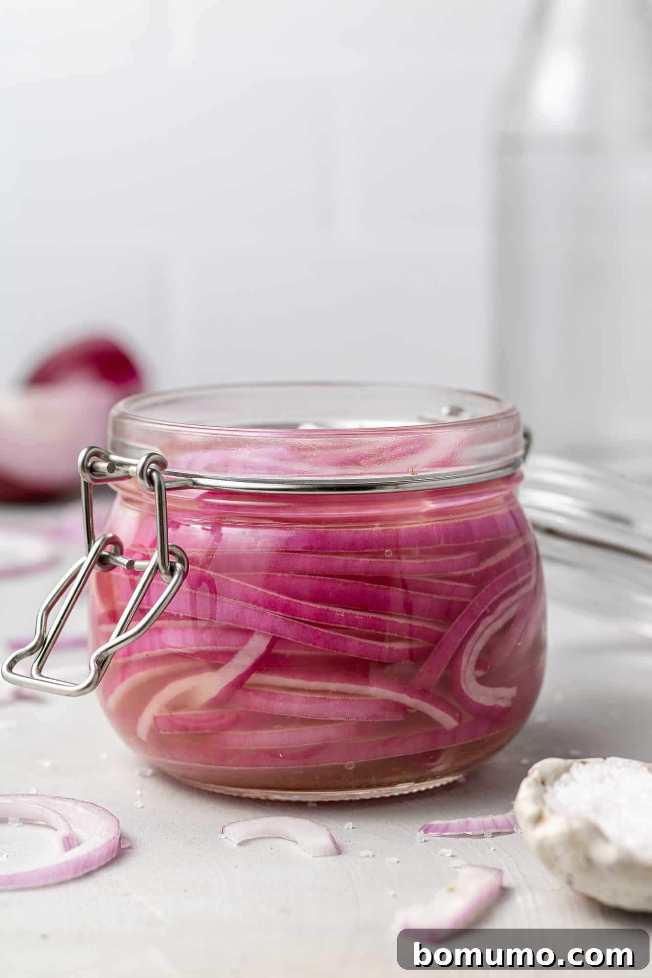 Beautifully pink sliced red onions submerged in pickling solution in a small glass jar, ready to eat.